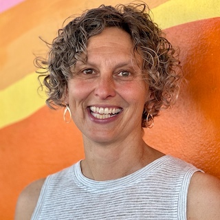 Portrait of a msiling woman with curly medium length hair in front of an abstract orange and yellow background